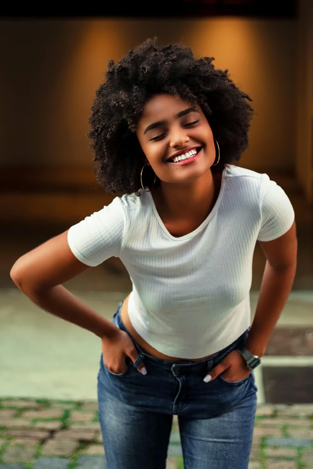 Fille noire et coupe afro en tee shirt blanc les mains sur les hanches dans les poches de son jean Levis fait un grand sourire ultra-brite
